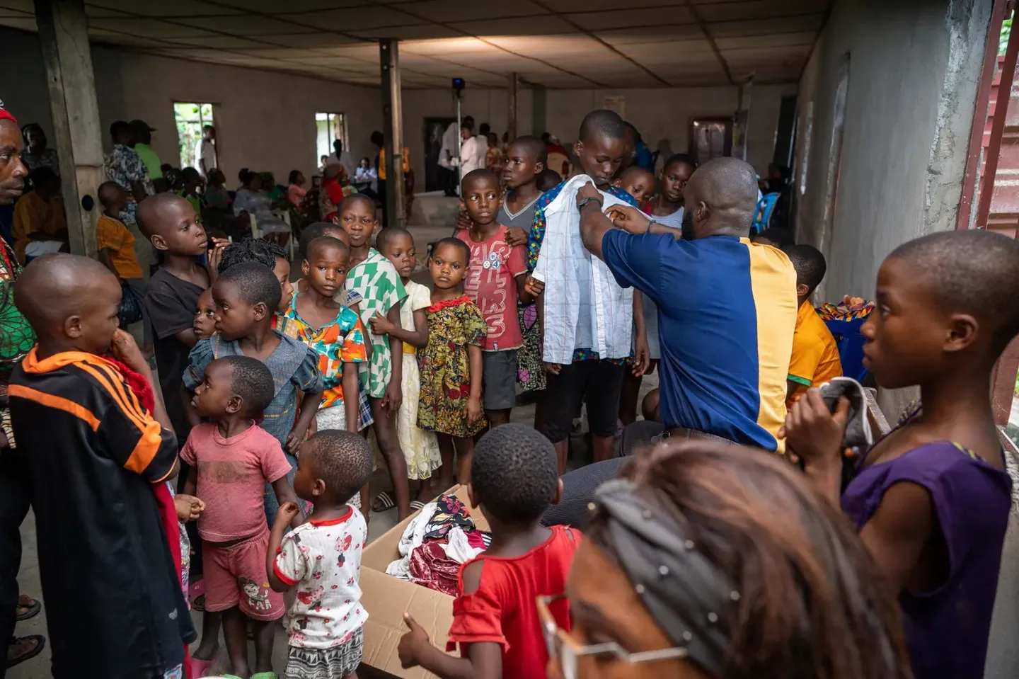 A GAMAID volunteer holds a shirt up against a boy to check the size as children wait in line