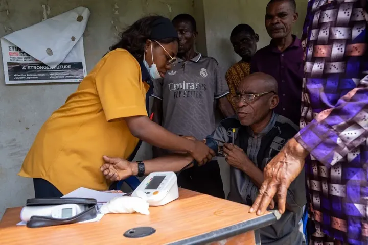 A GAMAID volunteer checks a man’s blood pressure at a community outreach as others wait