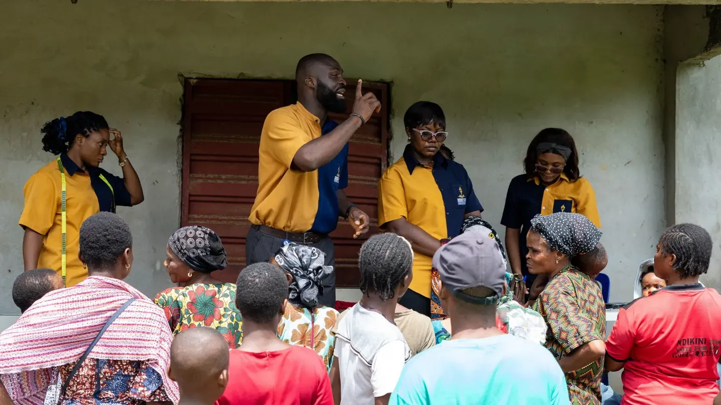 A GAMAID volunteer addresses villagers gathered outside the hall at Atan Ekpe, with three other volunteers beside him