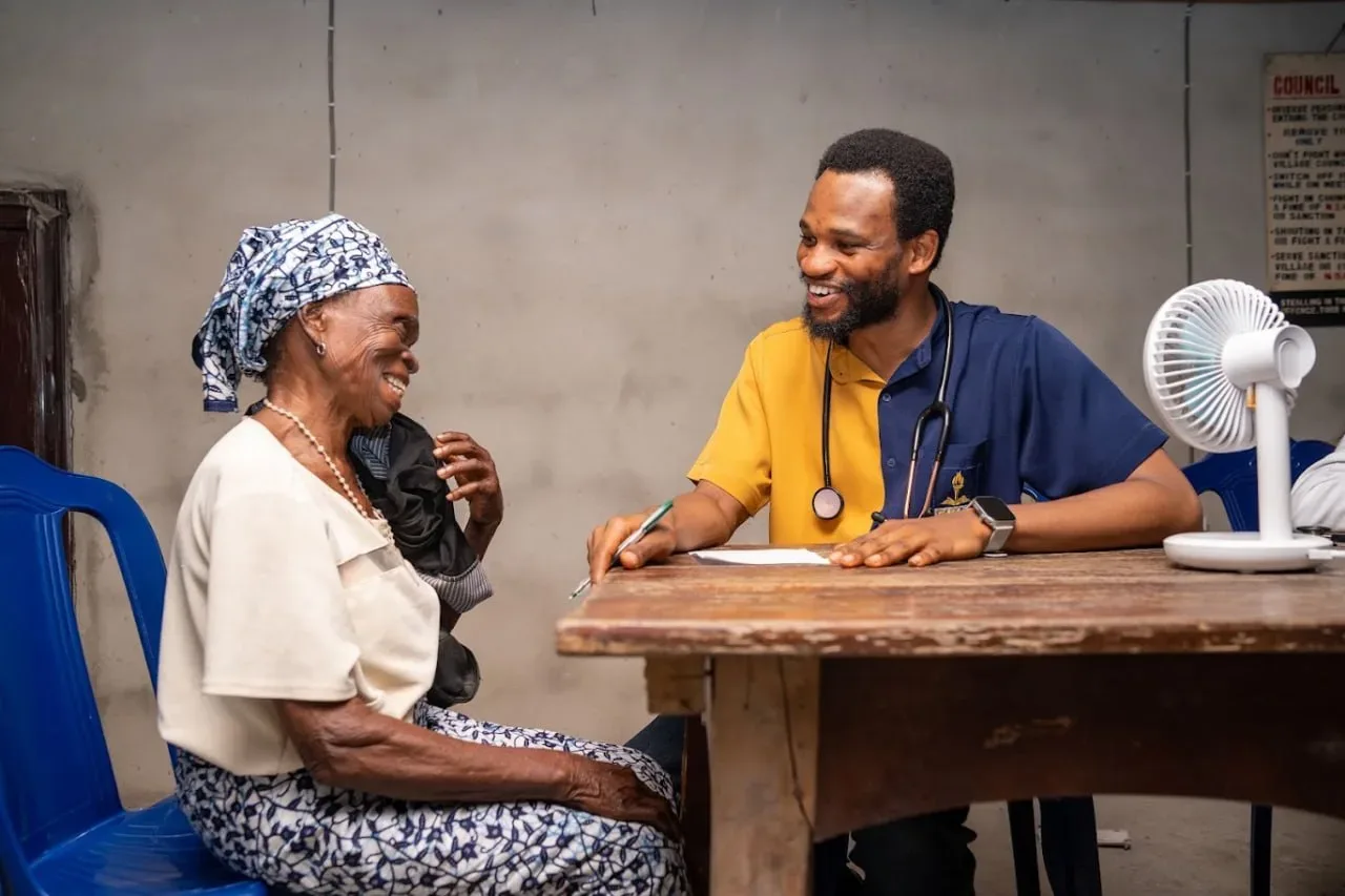 A GAMAID medical volunteer and an elderly woman share a laugh during a consultation at a community outreach
